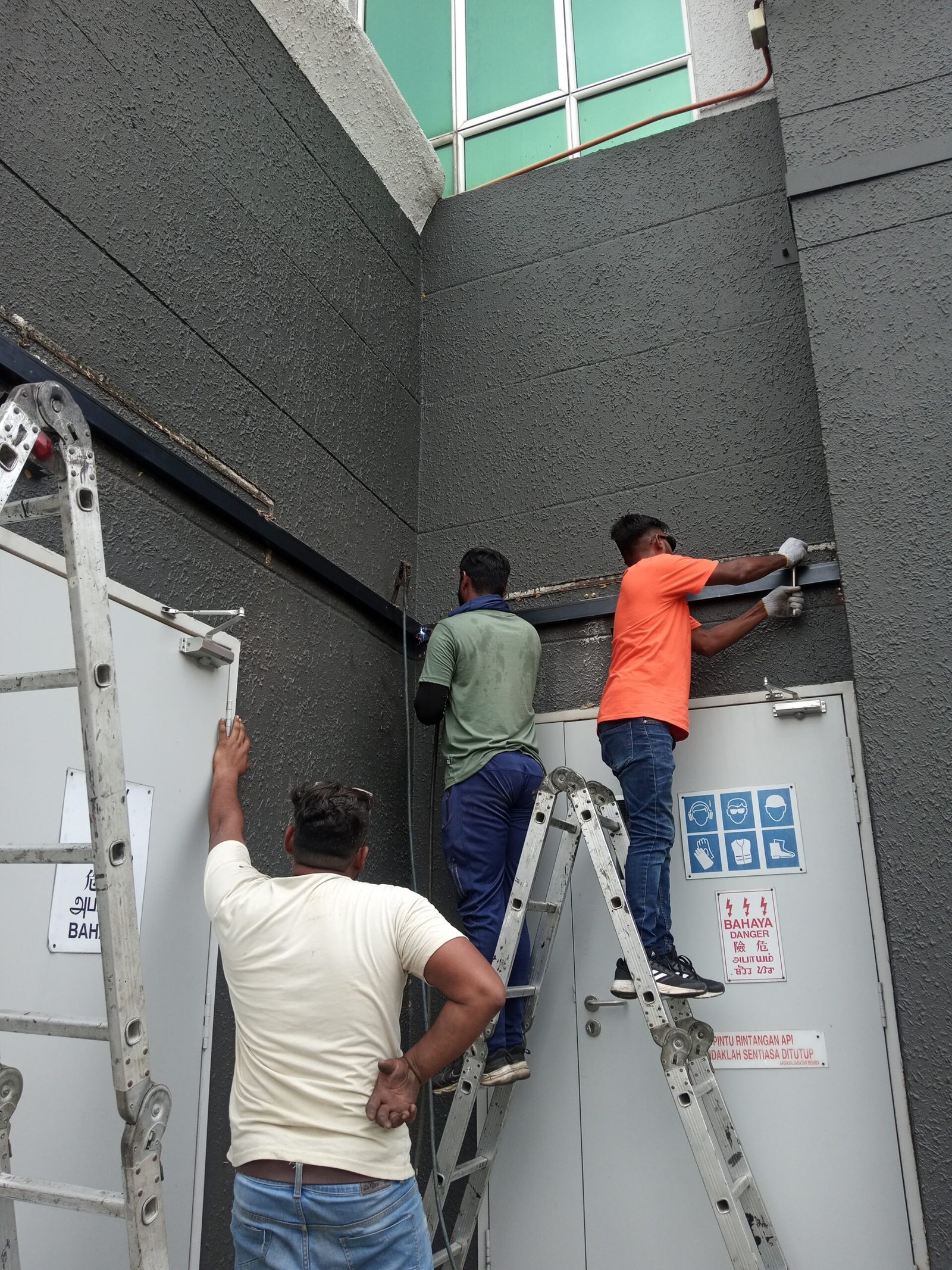 Workers installing a steel awning frame above service doors at a commercial building.