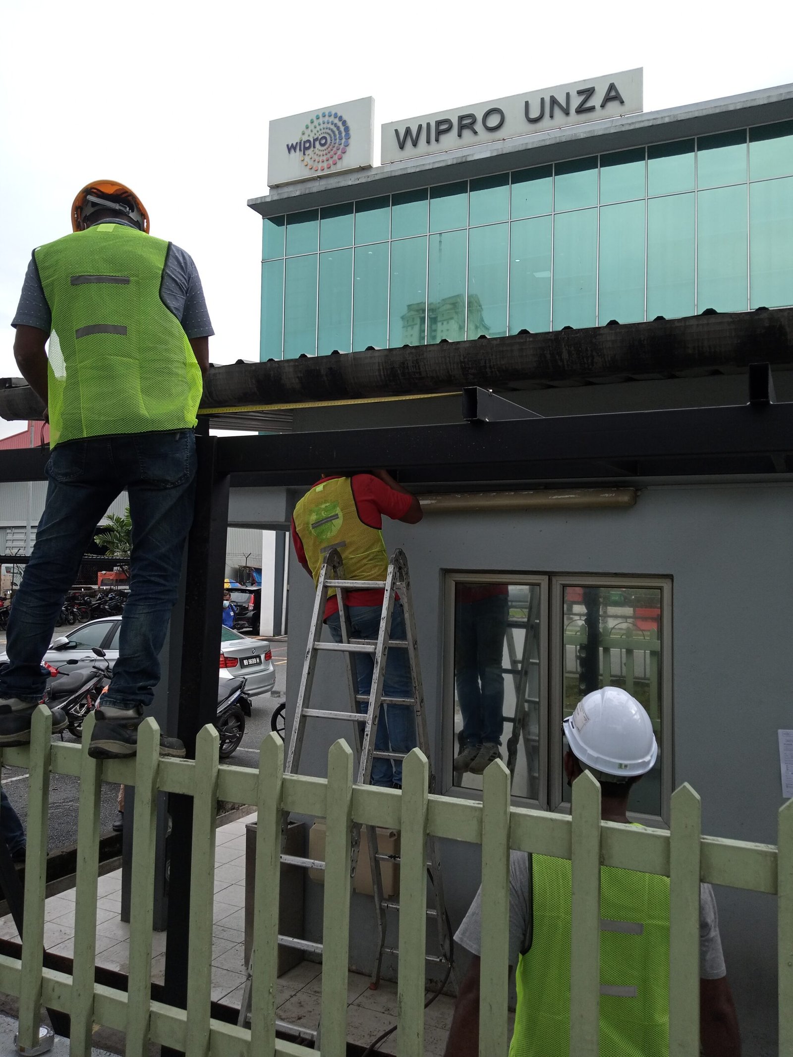 Workers in safety jackets and helmets installing the frame for an ACP guardhouse awning at Wipro in Subang Jaya, Selangor.